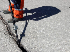 Worker applying crack sealant to asphalt pavement using a hot pour machine to prevent further surface damage