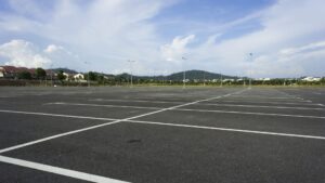 Freshly sealcoated and striped empty asphalt parking lot under a clear blue sky with residential buildings in the background