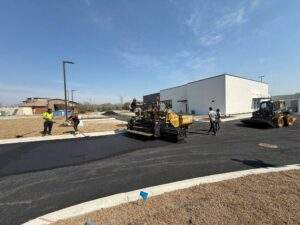 Asphalt paving crew installing a new roadway surface at a commercial development, using paving equipment and compact machinery to create a durable asphalt pavement.