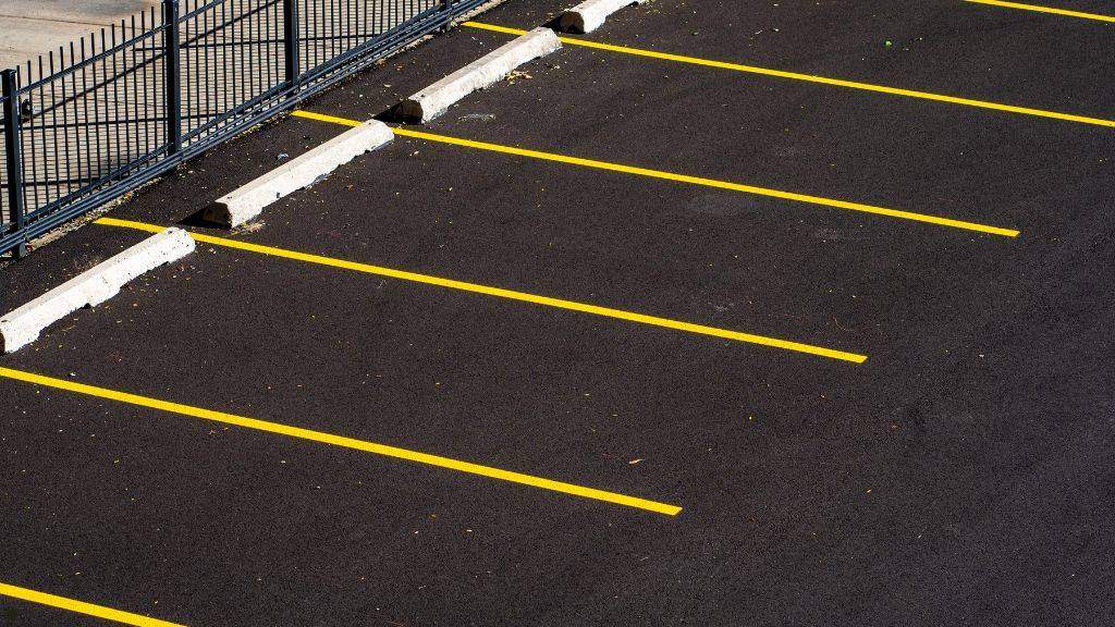 Empty commercial parking lot with fresh black sealcoating, crisp yellow line striping, and concrete wheel stops before winter weather arrives.